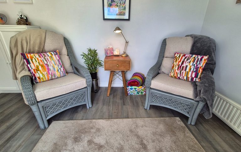 Therapy room seating area for therapist and client Two cosy armchairs with colourful cushions, a small table, and a rug on a wooden floor.